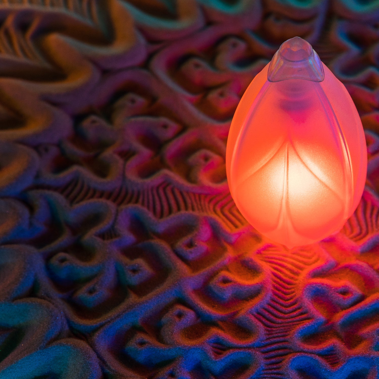 A single Flowtoys Podpoi v2 glowing softly on a psychedelic patterned rug
