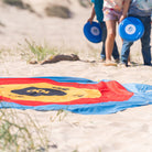 Scoring mat on sand with people holding frisbees in the background
